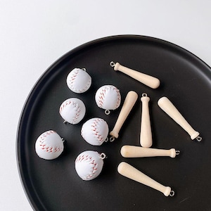May include: A collection of white baseball charms with red stitching and wooden baseball bat charms. The charms are on a black surface.