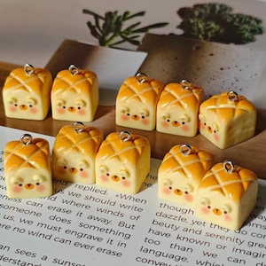 May include: A collection of miniature, charming bear-shaped bread charms. Each charm features a light yellow base with a cross-hatched orange top, a silver loop, and a cute bear face. These are ideal for jewelry making or crafting.