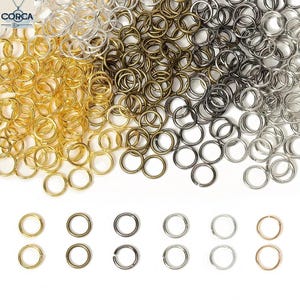 Op de afbeelding: Een assortiment van verbindingsringen in goud, antiek messing, gunmetal en zilver. De verbindingsringen zijn in een stapel gerangschikt, met een paar sets individuele ringen eronder. Deze sieradenbenodigdheden zijn perfect voor knutselen.
