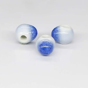 May include: Three blue and white ceramic beads with a hole in the center. The beads are oval shaped and have a gradient of blue to white.