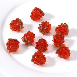 Peut inclure: Dix petites perles de verre en forme de fraises. Les perles sont rouges et ont une surface texturée.