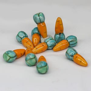 May include: A group of 10 ceramic carrot-shaped beads with blue and green painted details. The beads are a mix of orange and green colors.