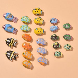 May include: A collection of 24 ceramic fish beads in various colours and designs, including blue, yellow, orange, green, black, and white. The beads are perfect for jewellery making, crafts, and home decor.