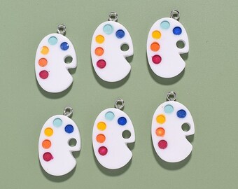 May include: Six white paint palette charms with colourful paint dots. The charms have a silver loop for hanging.