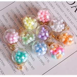 May include: Ten glass charm pendants with gold-colored metal rings. Each pendant contains colorful, small, round beads. The beads are in various colors, including pink, white, light blue, light green, light yellow, and purple.