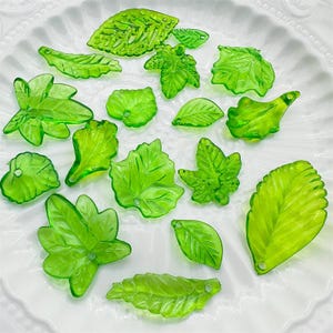 Pode incluir: Conjunto de pingentes de vidro em forma de folha verde. Os pingentes são translúcidos e têm um acabamento ligeiramente fosco. São perfeitos para adicionar um toque de natureza a joias ou artesanato.