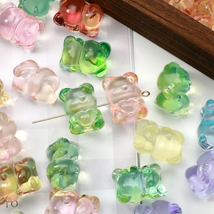 May include: A collection of colorful, translucent gummy bear-shaped beads in various shades of pink, green, yellow, and blue. Each bead has a heart-shaped detail. A thin metal wire runs through some of the beads.