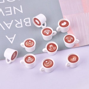 Può includere: Dieci tazze da caffè in ceramica bianca in miniatura con disegni di caffè marrone e latte art. I disegni includono cuori, foglie e vortici.