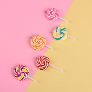 May include: Five colorful swirl lollipop charms with white sticks. The lollipops are pink and white, green and yellow, orange and yellow, red and white, and purple and yellow.