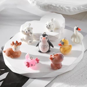 May include: A set of nine charm pendants featuring various animal designs, including a penguin, a polar bear, a deer, a duck, a swan, and an axolotl. The charms are made of white, brown, pink, yellow, and blue resin and have silver jump rings.