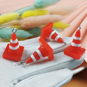 May include: Three red and white traffic cone charms with silver loops. The cones are made of resin and have a flat base.