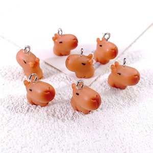May include: Six brown capybara charms with silver jump rings. The charms are made of polymer clay and are approximately 2.5 cm tall.
