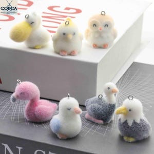May include: A collection of plush bird ornaments in various colors, including yellow, pink, white, and blue. Each ornament has a small metal loop for hanging. The birds include a duck, flamingo, owl, and other avian figures.