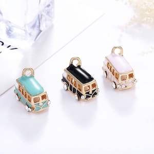 May include: Three charm pendants shaped like vintage buses. The buses are painted in different colors: turquoise, black, and pink. Each bus has white accents and gold trim. The charms are perfect for adding a touch of whimsy to jewelry.