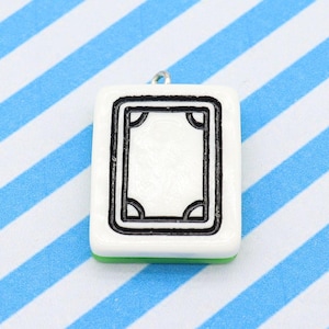 May include: A white square pendant with a black border and a central design, resembling a Mahjong tile. The pendant has a small silver loop at the top for hanging and a green base. The background features blue and white stripes.