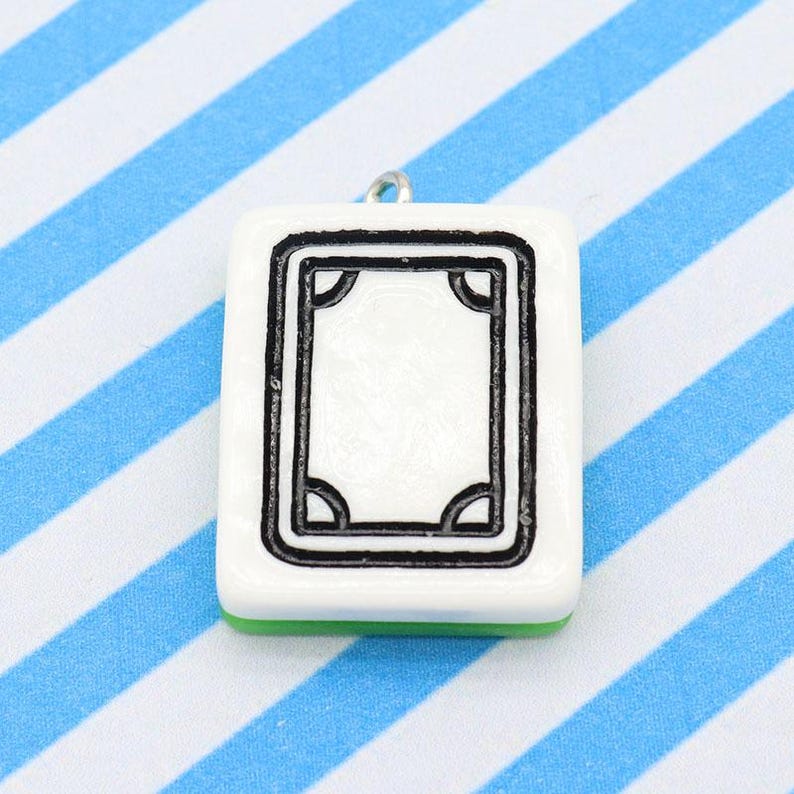 May include: A white square pendant with a black border and a central design, resembling a Mahjong tile. The pendant has a small silver loop at the top for hanging and a green base. The background features blue and white stripes.