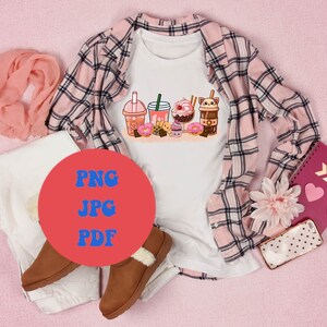 Peut inclure: Un t-shirt blanc avec un motif graphique de boissons et de beignets en dessin anim&eacute;. Le t-shirt est pos&eacute; sur une surface rose avec une chemise &agrave; carreaux, un pantalon blanc, une &eacute;charpe rose, un carnet, un t&eacute;l&eacute;phone et une paire de bottes marron.
