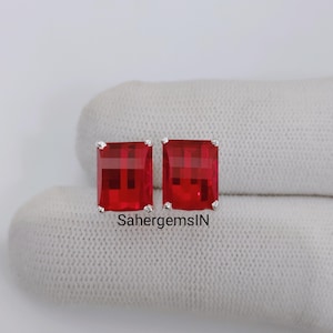 May include: Two rectangular red gemstone earrings with silver settings. The earrings are presented on a white surface. The text "SahergemsIN" is visible on the surface.