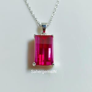 May include: A silver necklace featuring a rectangular, fuchsia-coloured pendant. The pendant is a large, faceted gemstone with a bright, reflective surface. The chain is delicate and hangs from a small bail attached to the pendant. The text "SahergemsIN" is visible.