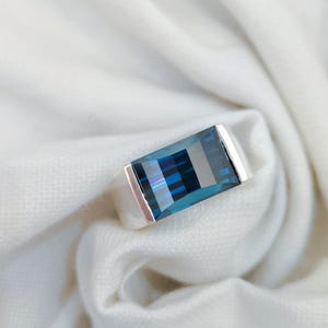May include: A silver ring featuring a large, rectangular, blue gemstone.