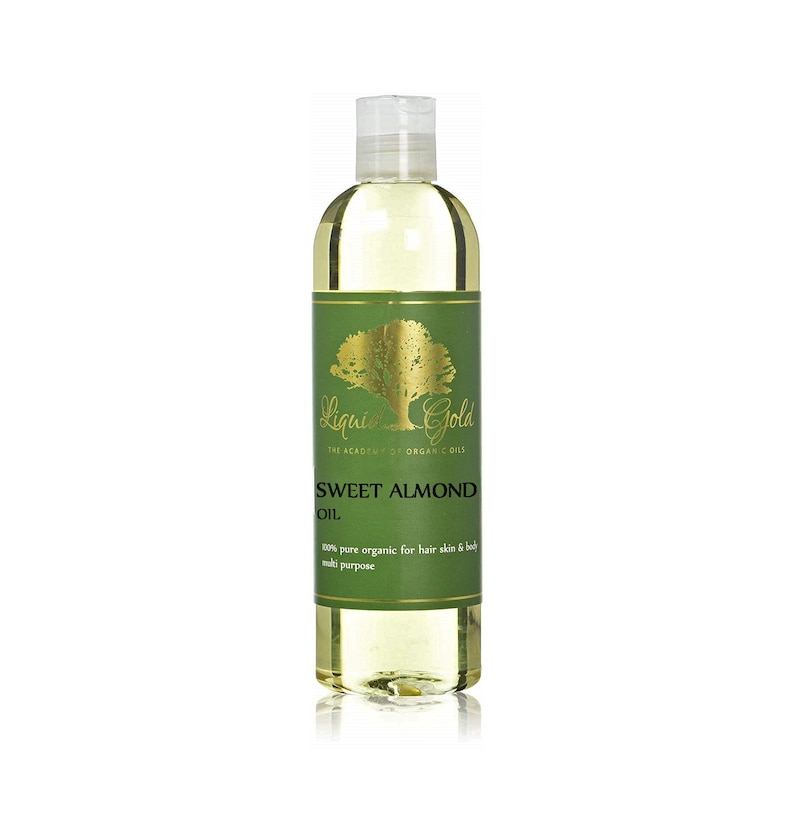 Puede incluir: Una botella de vidrio transparente de aceite de almendras dulces Liquid Gold. La botella tiene una etiqueta dorada con un &aacute;rbol verde y el texto "Liquid Gold The Academy of Organic Oils Sweet Almond Oil 100% pure organic for hair skin & body multi purpose".