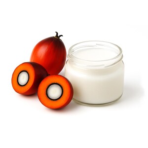 May include: A jar of white liquid next to two halves of a palm fruit and a whole palm fruit. The palm fruit halves have a bright orange exterior with a white center. The whole fruit is a deep red color.