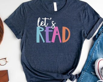 May include: A navy blue t-shirt with the text "let's READ" in colorful letters. The shirt is tied in a knot and is displayed with a pair of jeans and white sneakers.
