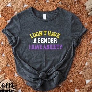 May include: A dark gray t-shirt with the text "I don't have a gender I have anxiety" in yellow and purple lettering.