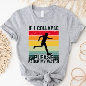 May include: A gray t-shirt with the text "IF I COLLAPSE PLEASE PAUSE MY WATCH" and a silhouette of a runner. The text is above a retro-style design with red, orange, yellow, and green stripes.