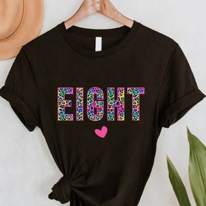 May include: Black t-shirt with the word "EIGHT" in rainbow leopard print letters and a pink heart.