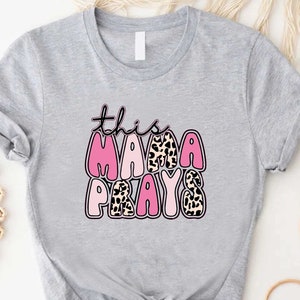 May include: Gray t-shirt with a pink and leopard print design that says "this mama prays".