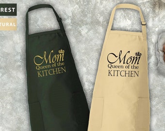 May include: Two kitchen aprons with the text "Mom Queen of the Kitchen" in gold lettering. The apron on the left is dark green and the apron on the right is beige.
