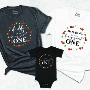 May include: Three t-shirts with a strawberry theme. The adult shirts say "Daddy of the berry sweet one" and "Mama of the berry sweet one". The baby shirt says "The berry sweet one".