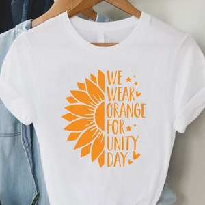 May include: White t-shirt with a sunflower graphic and the text "We wear orange for unity day".
