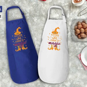 Op de afbeelding: Twee keukenschorten met een ontwerp van een heksenhoed en laarzen. De tekst op de schorten luidt "Kitchen witch stirring up magic". Een schort is koninklijkblauw en de andere is wit.