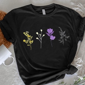 May include: Black t-shirt with a graphic of five stylized flowers in yellow, green, purple, and gray. The flowers are arranged in a row across the center of the shirt.