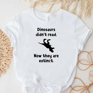 May include: White t-shirt with a black dinosaur graphic and the text "Dinosaurs didn't read. Now they are extinct."