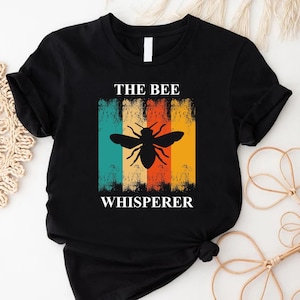 May include: Black t-shirt with a retro-style graphic of a bee and the text "THE BEE WHISPERER".