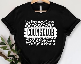 May include: Black t-shirt with a white leopard print design and the word "COUNSELOR" in white text.