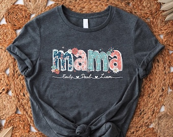 May include: A dark gray t-shirt with the word "mama" in colorful floral letters. The names "Emily, Paul, Liam" are written below the word "mama" in a smaller font.