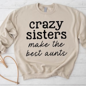 May include: A beige sweatshirt featuring the black text "crazy sisters make the best aunts". The long-sleeved sweatshirt has a crew neck. The text is in a bold, sans-serif font.