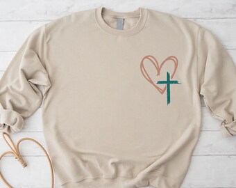 May include: A beige sweatshirt with a pink heart and a green cross graphic design.