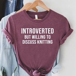 May include: A maroon t-shirt with the text "Introverted but willing to discuss knitting" in white.