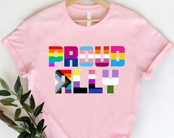 Puede incluir: Camiseta rosa con el texto "PROUD ALLY" en colores arcoíris. Cada letra está formada por diferentes banderas del orgullo.