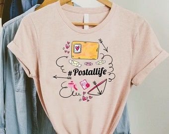 May include: A pink t-shirt with a graphic design featuring a yellow envelope, pink hearts, and the text "#Postallife".