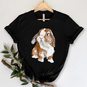 K&ouml;nnte beinhalten: Schwarzes T-Shirt mit einer Illustration eines braunen und wei&szlig;en Kaninchens.