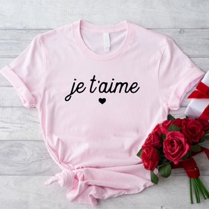 May include: Pink t-shirt with the text "je t'aime" in black cursive lettering and a small black heart.
