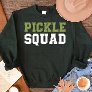 May include: A dark green sweatshirt with the text "Pickle Squad" in white and green letters.