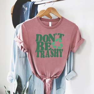 May include: A pink t-shirt with the text "DON'T BE TRASHY" in green letters with a green recycling symbol in the middle of the word "BE".