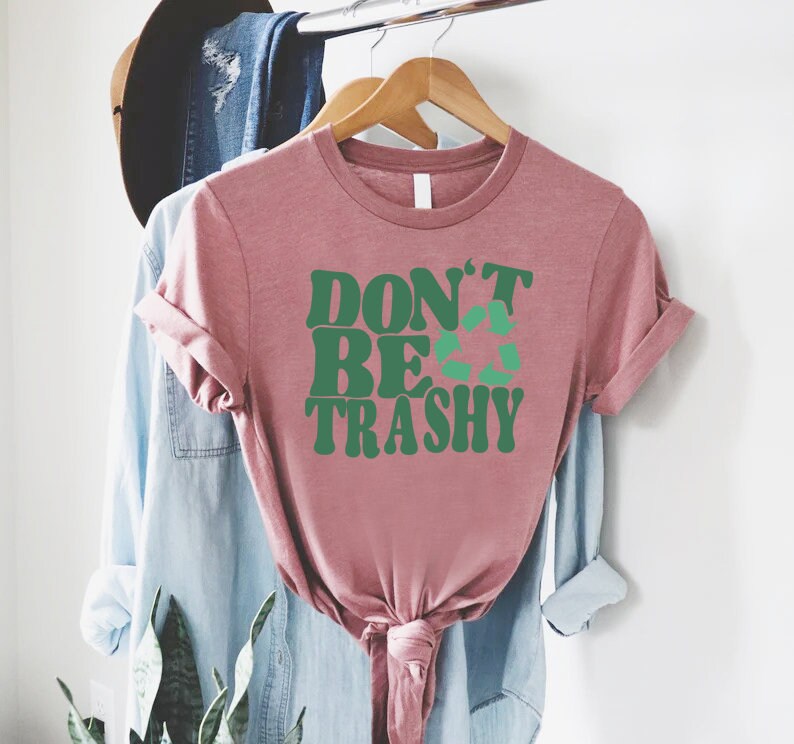 May include: A pink t-shirt with the text "DON'T BE TRASHY" in green letters with a green recycling symbol in the middle of the word "BE".